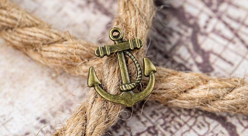 Small anchor pin, resting on rope, on top of a map